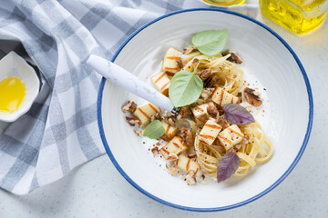 Creamy pasta served with haloumi cheese and walnuts in a white plate, horizontal shot, elevated view