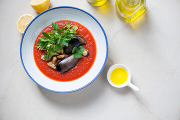 Plate of tomato cream-soup with mussels on a beige stone background, horizontal shot with copyspace, above view