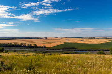 Beautiful panoramic view of ripe wheat fields, valley with river and meadow and beautiful sky.