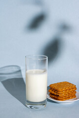 a glass of yogurt and a stack of cookies on a blue background with a shadow, a morning snack