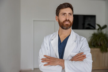 Fototapeta premium Portrait of handsome doctor in uniform standing in medicine clinic hall and looking away
