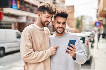 Young couple using smartphone hugging each other at street