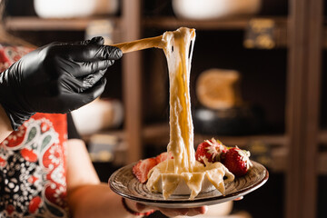 Eating hot baked camembert cheese with grissini sticks. Stretching melted Camembert cheese Italian traditional delicacy.