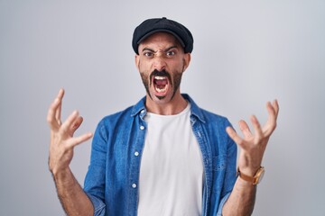 Hispanic man with beard standing over isolated background crazy and mad shouting and yelling with...