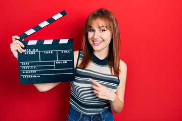 Redhead young woman holding video film clapboard smiling happy pointing with hand and finger