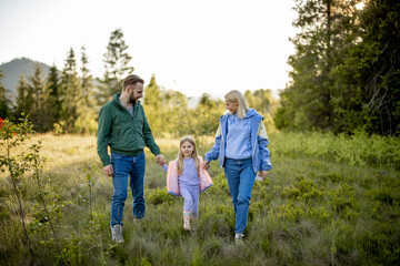 Fototapeta premium Young caucasian couple with little girl walk together while traveling in the mountains. Happy family spending summer vacation on nature