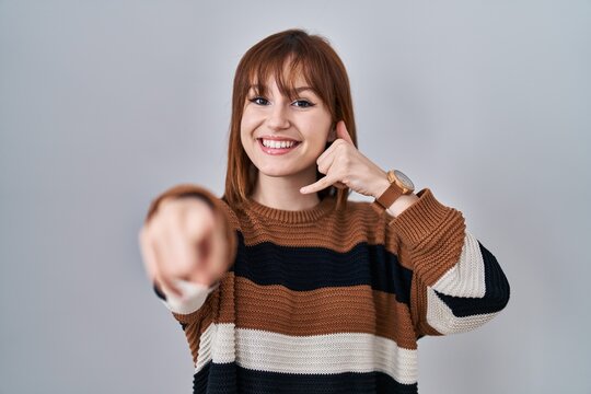 Young beautiful woman wearing striped sweater over isolated background smiling doing talking on the telephone gesture and pointing to you. call me.