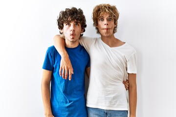 Fototapeta premium Young gay couple standing together over isolated background making fish face with lips, crazy and comical gesture. funny expression.