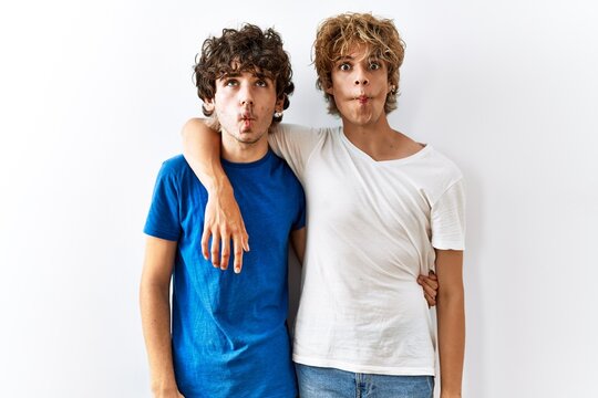 Young gay couple standing together over isolated background making fish face with lips, crazy and comical gesture. funny expression.