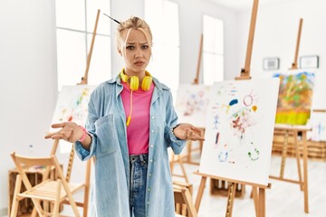 Young caucasian girl at art studio clueless and confused with open arms, no idea concept.