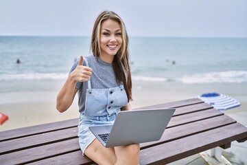 Young caucasian woman working using computer laptop outdoors smiling happy and positive, thumb up doing excellent and approval sign