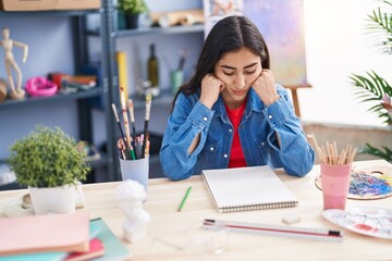 Young hispanic girl artist sitting on desk with doubt expression at art studio
