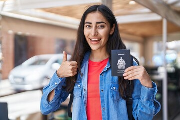 Young teenager girl holding canada passport smiling happy and positive, thumb up doing excellent...