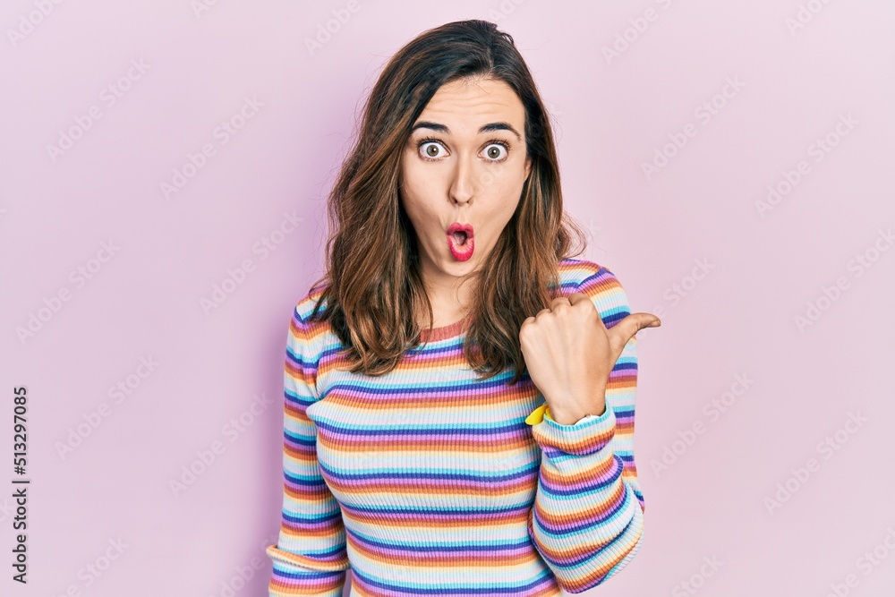 Poster Young hispanic girl wearing casual clothes surprised pointing with hand finger to the side, open mouth amazed expression.