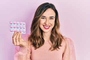 Young hispanic girl holding pills looking positive and happy standing and smiling with a confident smile showing teeth