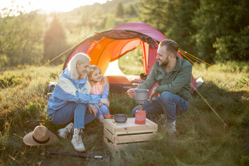 Couple with little girl have picnic at campsite while traveling with tent in the mountains. Young...