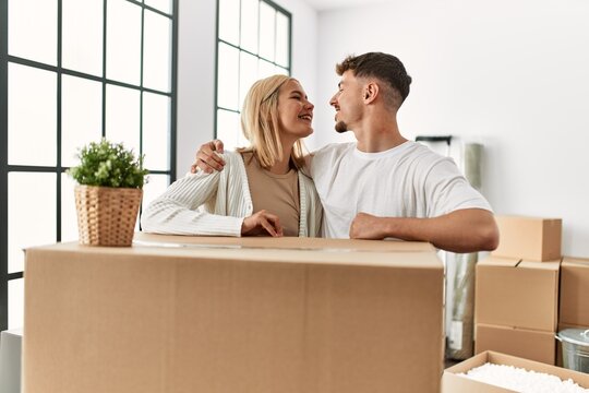 Young caucasian couple smiling happy and hugging leaning on carboard box at new home.