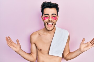 Young hispanic man shirtless wearing towel and eye bags patches celebrating mad and crazy for...