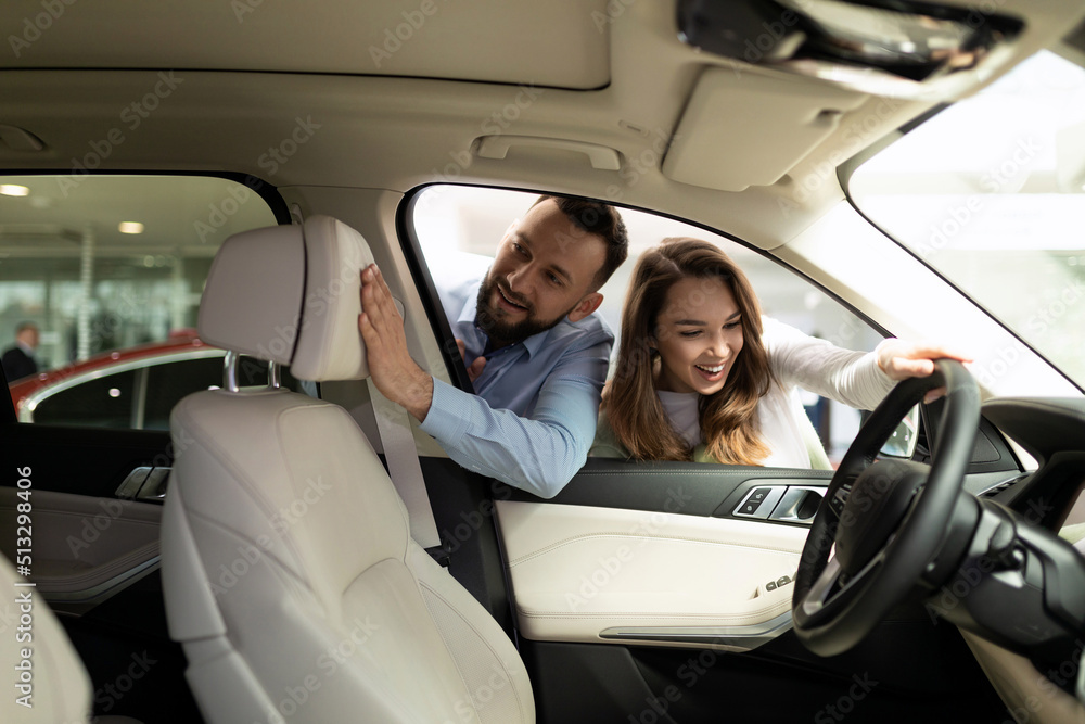 Wall mural a young married couple examines with interest the features of the interior of a new car in a car dea