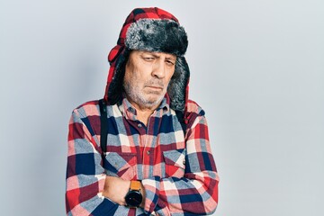 Handsome mature man wearing winter hat with ear flaps skeptic and nervous, disapproving expression on face with crossed arms. negative person.