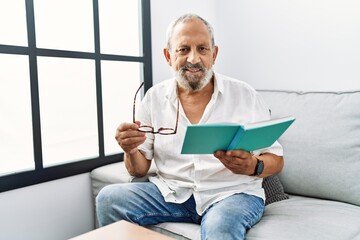 Senior grey-haired man smiling confident reading book at home