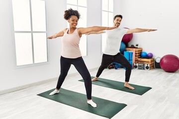 Fototapeta na wymiar Young african american woman and hispanic man exercising at pilates room, stretching body and doing yoga pose, training strength and balance