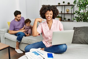 Mother of interracial family working using computer laptop at home looking confident with smile on face, pointing oneself with fingers proud and happy.