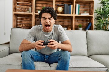 Young hispanic man playing video game sitting on the sofa at home.
