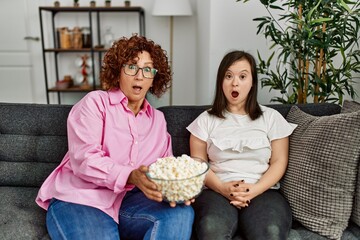 Mature mother and down syndrome daughter at home eating popcorn and watching television