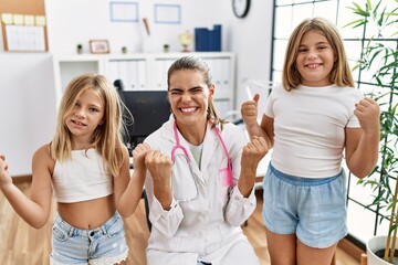 Pediatrician woman working at the clinic with two little girls screaming proud, celebrating victory...