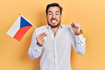 Handsome caucasian man with beard holding czech republic flag screaming proud, celebrating victory and success very excited with raised arm