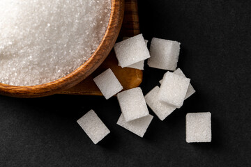 Granulated sugar and sugar cubes in wooden bowl on dark background