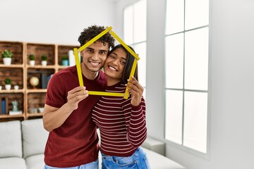 Young latin couple smiling happy holding house project at home.