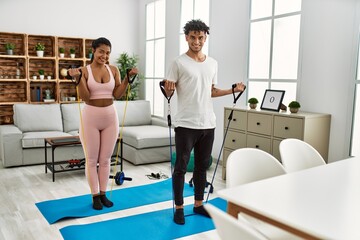 Young latin couple smiling happy training using elastic band at home.