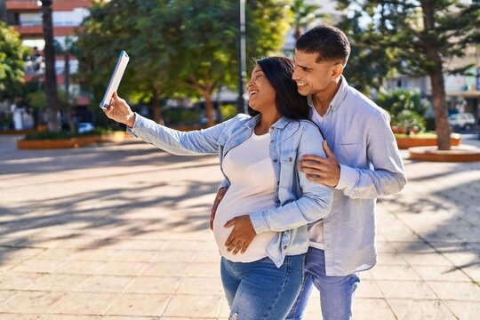 Young latin couple expecting baby making selfie by the touchpad at park