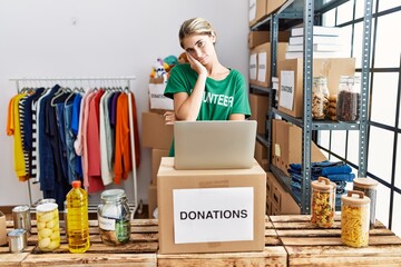 Young blonde woman wearing volunteer t shirt at donations stand thinking looking tired and bored with depression problems with crossed arms.