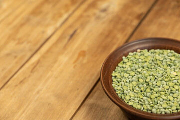 Dry split peas in a bowl against a wooden background. Green pea beans in brown earthenware bowl. Uncooked food. Healthy food. Close-up. Selective focus. Copy space for text and design elements.