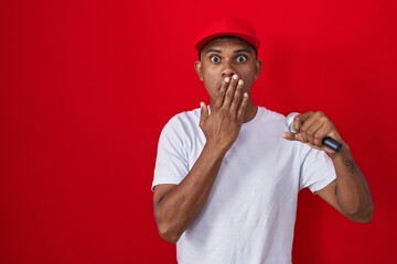 Young hispanic man singing song using microphone covering mouth with hand, shocked and afraid for...