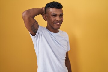 Fototapeta na wymiar Young hispanic man standing over yellow background smiling confident touching hair with hand up gesture, posing attractive and fashionable