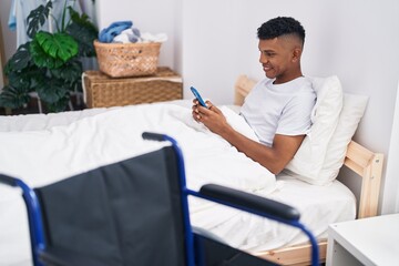 Young latin man using smartphone lying on bed at bedroom