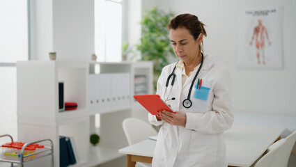 Middle age hispanic woman wearing doctor uniform using touchpad at clinic