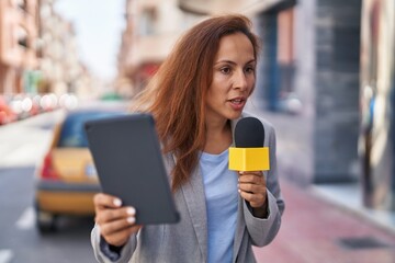Young woman reporter working using microphone and touchpad at street