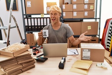 Young blond man drinking coffee working at online shop celebrating achievement with happy smile and winner expression with raised hand