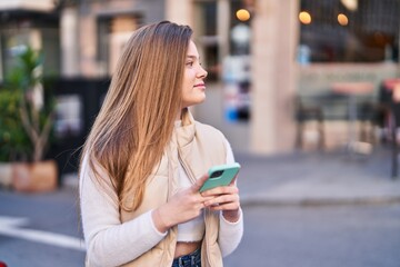 Young blonde woman smiling confident using smartphone at street