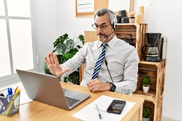 Naklejka premium Middle age hispanic business man working at the office wearing operator headset doing stop sing with palm of the hand. warning expression with negative and serious gesture on the face.
