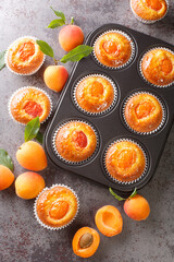 Muffins with fresh apricots close-up in a muffin pan on the table. Vertical top view from above