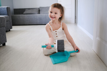 Cute European child with blue scoop for garbage and brush for sweeping floor helps to clean, help around house toddlers, development of Montessori