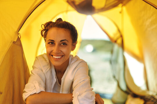 Close up beautiful face of emotionally smiling woman inside tent during vacation or weekend, enjoys free camping life