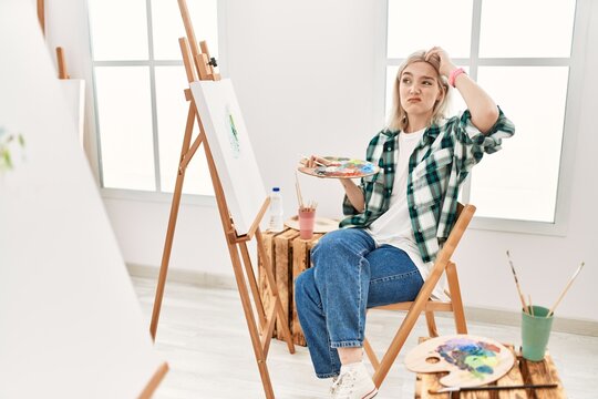 Young artist woman painting on canvas at art studio confuse and wondering about question. uncertain with doubt, thinking with hand on head. pensive concept.