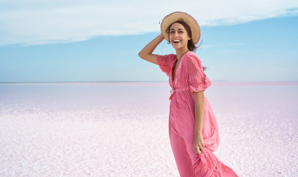 Beautiful excited woman emotionally smile, wearing elegant pink dress and hat, enjoying vacation at beach of pink lake. Ukraine Syvash lake